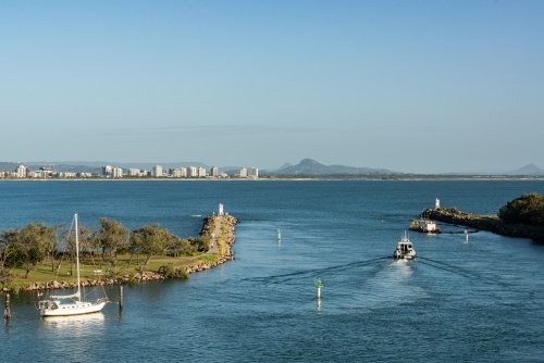People walking on groyne, boat motoring out through river mouth, high rise buildings and mountains - Australian Stock Image