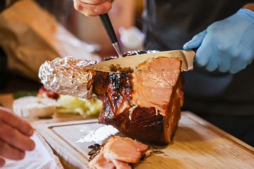 Person carving glazed Christmas ham on wooden cutting board - Australian Stock Image