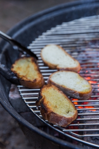 Person grilling thick slices of bread on hot coals on a bbq outside - Australian Stock Image