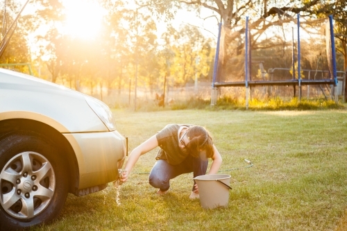 Person hand washing front of family car in backyard in natural light flare - Australian Stock Image