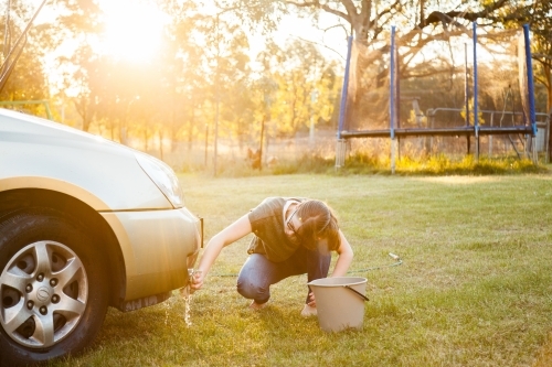 Person hand washing front of family car in backyard in natural light flare