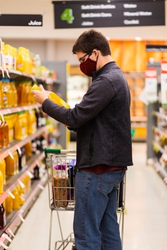 person in grocery store aisle buying juice wearing home made face mask during covid-19 pandemic - Australian Stock Image