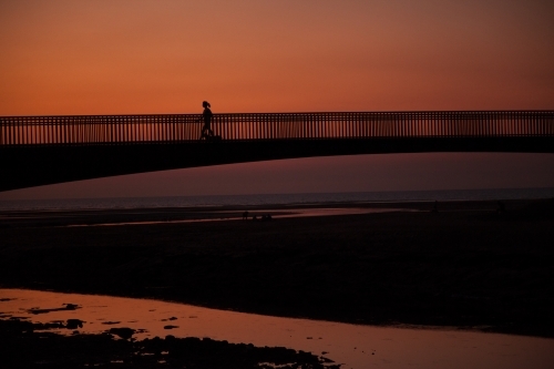 Person jogging across bridge at sunset
