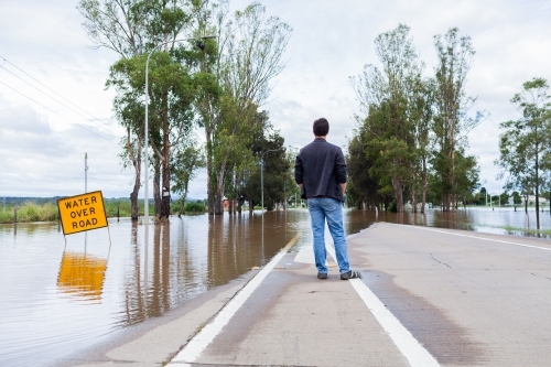 Person looking at floodwaters over road cutting off access via New England Highway through singleton - Australian Stock Image