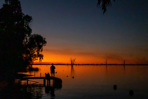 Person on jetty in front of sunset over lake - Australian Stock Image