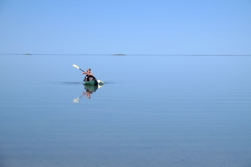 Person paddling kayak on flat glassy ocean - Australian Stock Image