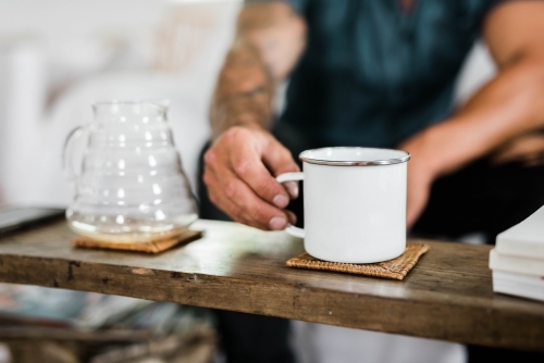 Person picking up a cup of coffee next to a pour over vessel - Australian Stock Image