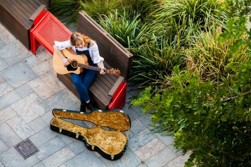 Person playing guitar on street footpath busking - Australian Stock Image