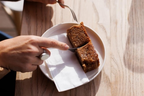 Person slicing up banana bread on a plate - Australian Stock Image