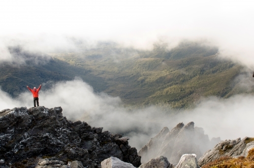 Person standing on a cliff in a misty mountain range - Australian Stock Image