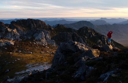 Person standing on cliff, looking out over mountain range - Australian Stock Image