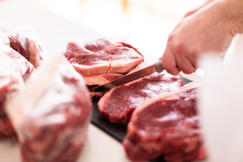 person using knife cutting beef steaks up for storage - Australian Stock Image