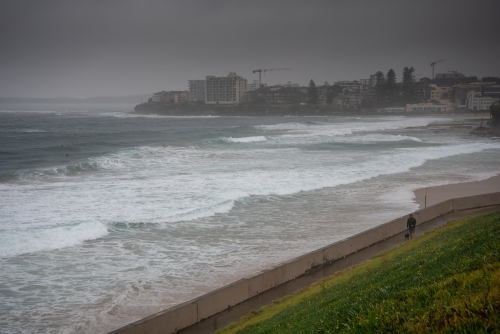 Person walking a dog in the rain along the beachside walking track in Cronulla - Australian Stock Image