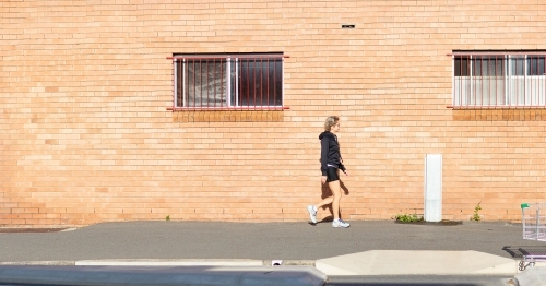 Person walking along footpath in front of brick building