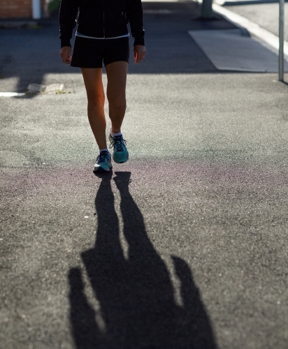 Person walking from waist down with long shadow in foreground - Australian Stock Image