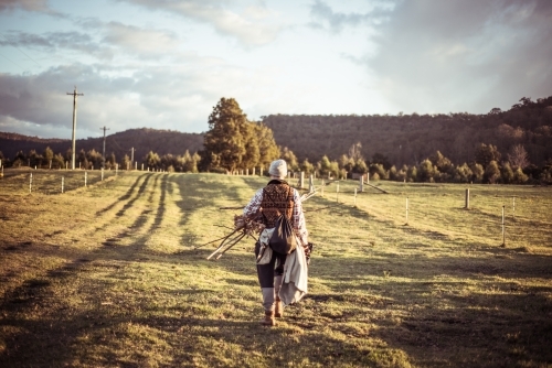 Person walking through paddock to campsite with kindling sticks for fire - Australian Stock Image