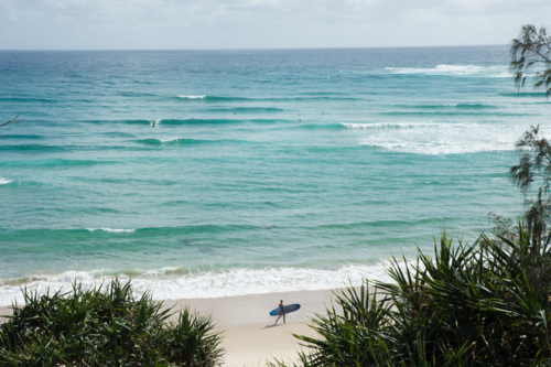 Person with surfboard on beach with ocean behind at Byron Bay - Australian Stock Image