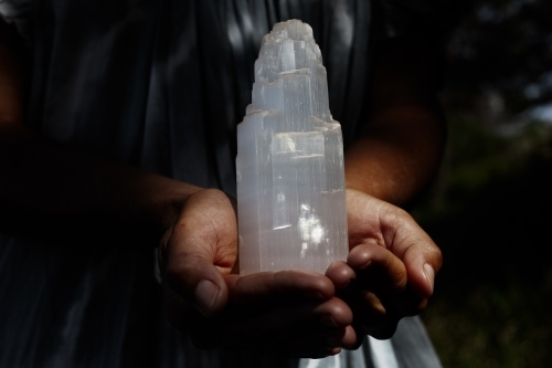 Persons hands holding gypsum tower crystal in moody, dark lighting