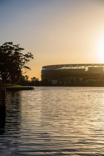 Perth AFL Stadium over water at sunset
