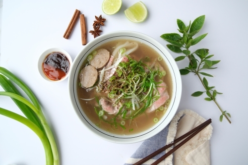 Pho noodle soup in a bowl with fresh herbs and spices on the surface. - Australian Stock Image