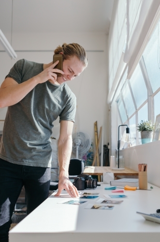Photographer with a man bun viewing photos while on the phone - Australian Stock Image