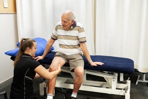 Physiotherapist healthcare worker talking with senior male client - Australian Stock Image
