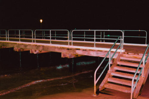 Pier glowing red with artificial light over dark coastal waters - Australian Stock Image