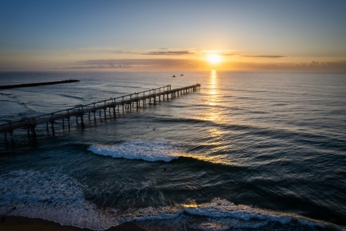 Pier going off in the distance with the sunrise over the ocean on a clear morning off the coast - Australian Stock Image