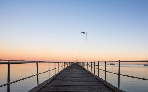 Pier leading out to the distance into the ocean on a clear dawn morning - Australian Stock Image