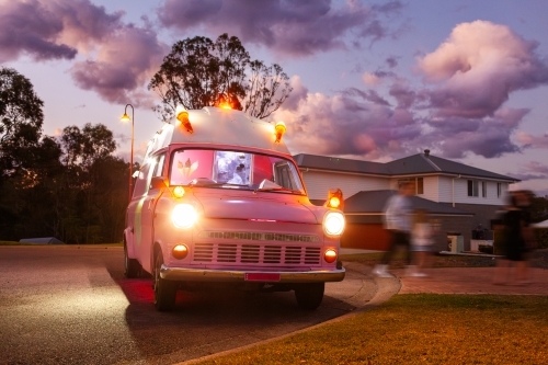 Pink Ice cream truck at dusk in suburban area with lights on selling ice-cream - Australian Stock Image