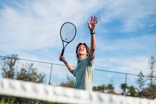 Player prepares to smash a tennis ball on a bright day at an outdoor court. - Australian Stock Image
