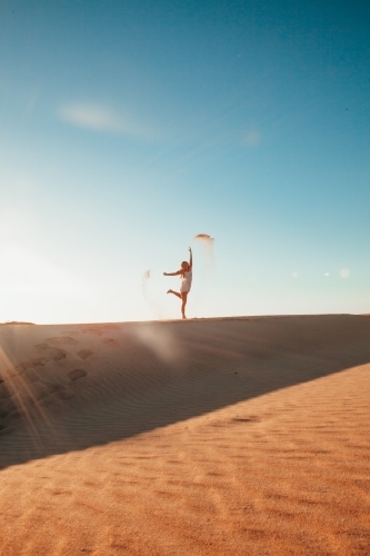 Playful young adult Tossing Sand on Sunlit Dunes during a summer sunset - Australian Stock Image