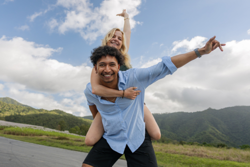 Polynesian man giving a Caucasian woman a piggyback ride on a country road - Australian Stock Image