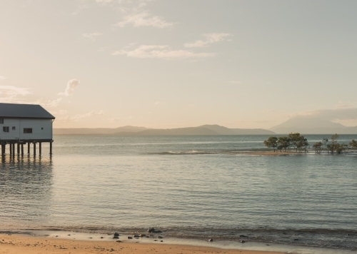 Port Douglas Sugar Wharf on stilts over the calm ocean in, with distant hills and beautiful dusk sky - Australian Stock Image