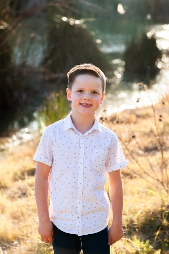Portrait if a smiling young boy outside beside dam - Australian Stock Image