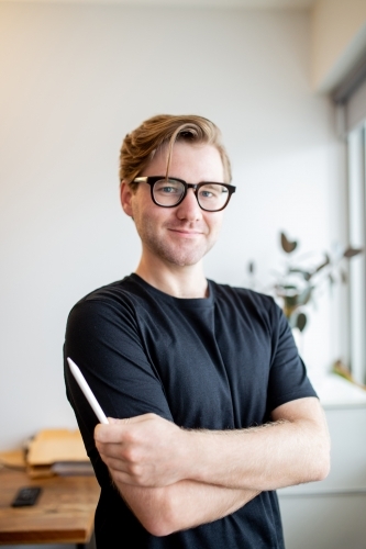 Man wearing glasses standing with a digital pencil in his hand in an office - Australian Stock Image
