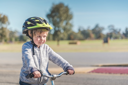 Portrait of a child wearing a helmet while riding his balance bike on track in Adelaide Parklands - Australian Stock Image
