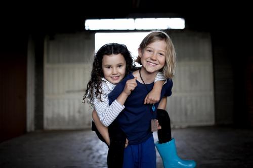 Portrait of a girl carrying her friend with background of dimly lit shed - Australian Stock Image