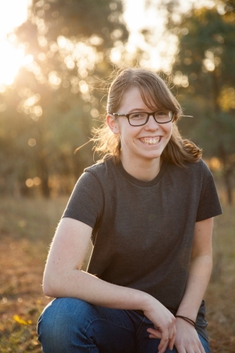 Portrait of a happy teenage girl with glasses smiling in rural country paddock at sunset - Australian Stock Image