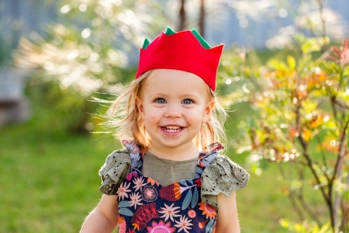 Portrait of a happy toddler girl outside in felt Christmas cracker hat - Australian Stock Image