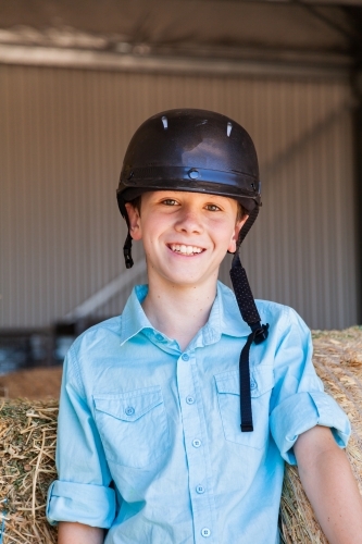 Portrait of a happy young boy on hay bales in a shed - Australian Stock Image