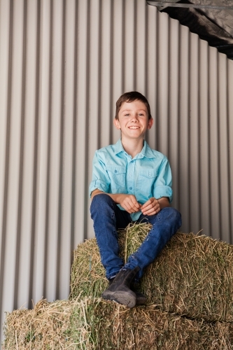 Portrait of a happy young boy on hay bales in a shed - Australian Stock Image