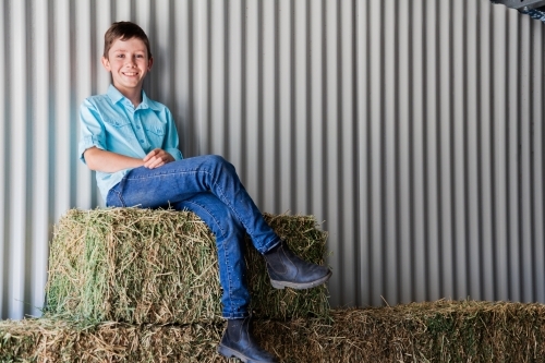 Portrait of a happy young boy on hay bales in a shed - Australian Stock Image