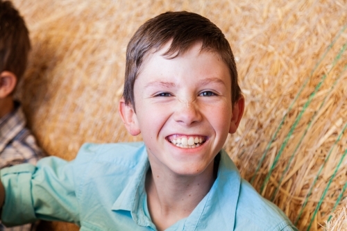 Portrait of a happy young boy on hay bales in a shed - Australian Stock Image