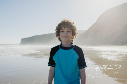 Portrait of a happy young boy with curly hair at the beach in the afternoon - Australian Stock Image