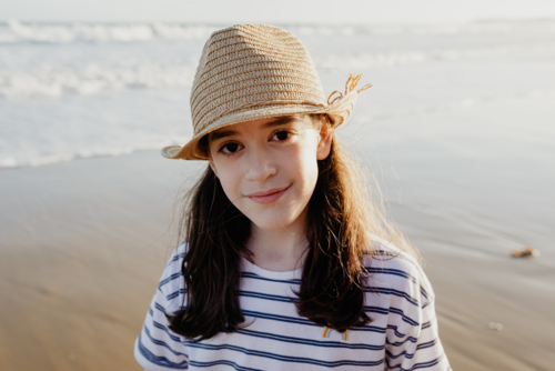 Portrait of a happy young girl wearing a sunhat at the beach in the afternoon - Australian Stock Image
