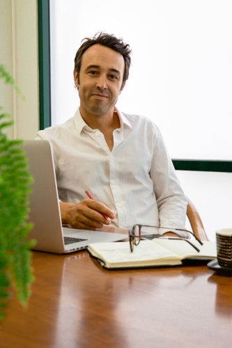 Portrait of a male office worker sitting with laptop and note book at a meeting table - Australian Stock Image