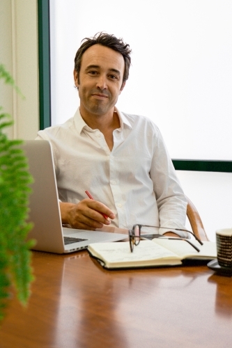 Portrait of a male office worker sitting with laptop and note book at a meeting table