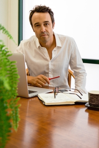 Portrait of a male office worker sitting with laptop and note book at a meeting table - Australian Stock Image