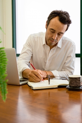 Portrait of a male office worker sitting with laptop and note book at a meeting table - Australian Stock Image